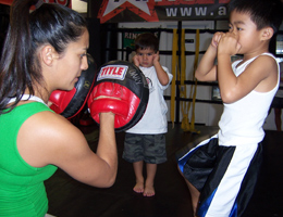 Coach Gina holding muay thai mitts for kids mixed martial arts class.